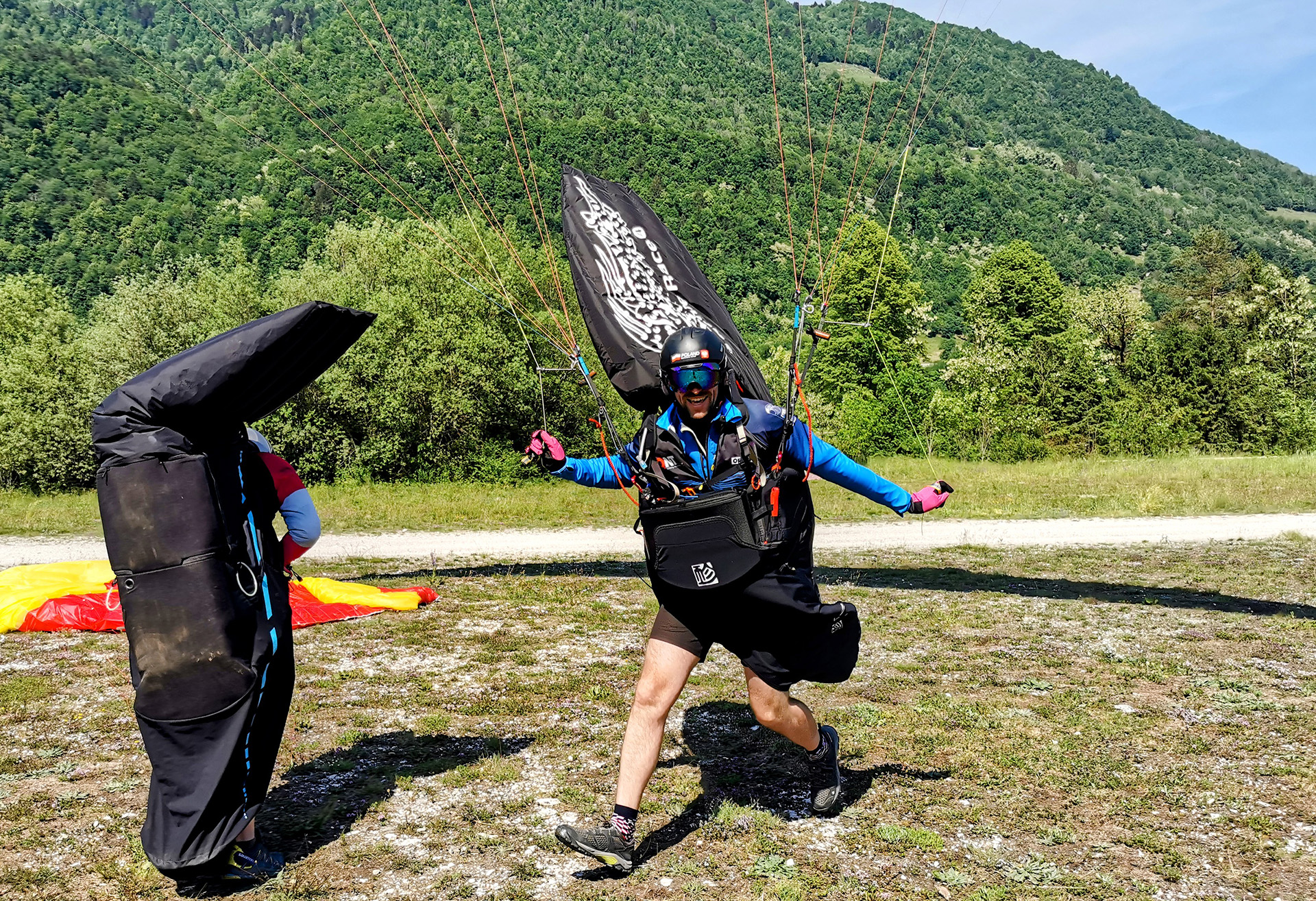 Pilot paralotni lądujący na łące obok innego pilota