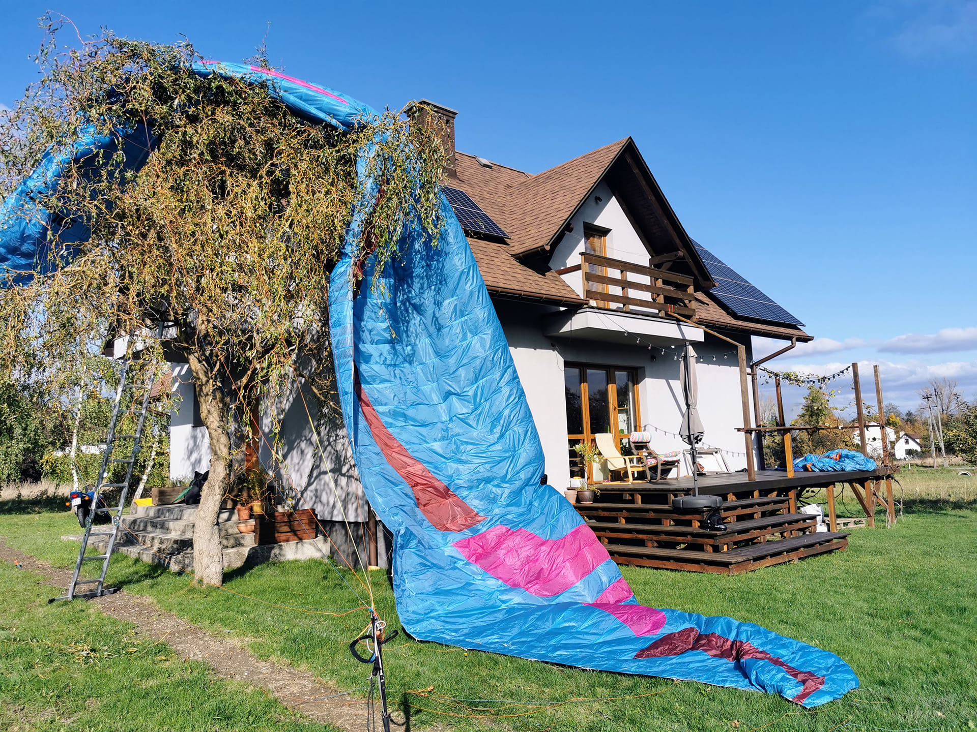 Niebieska paralotnia zawieszona na drzewie obok domu